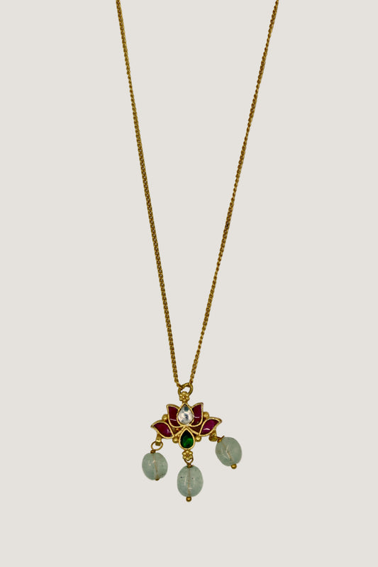 Gold necklace with a pendant featuring green and red stones on a light gray background